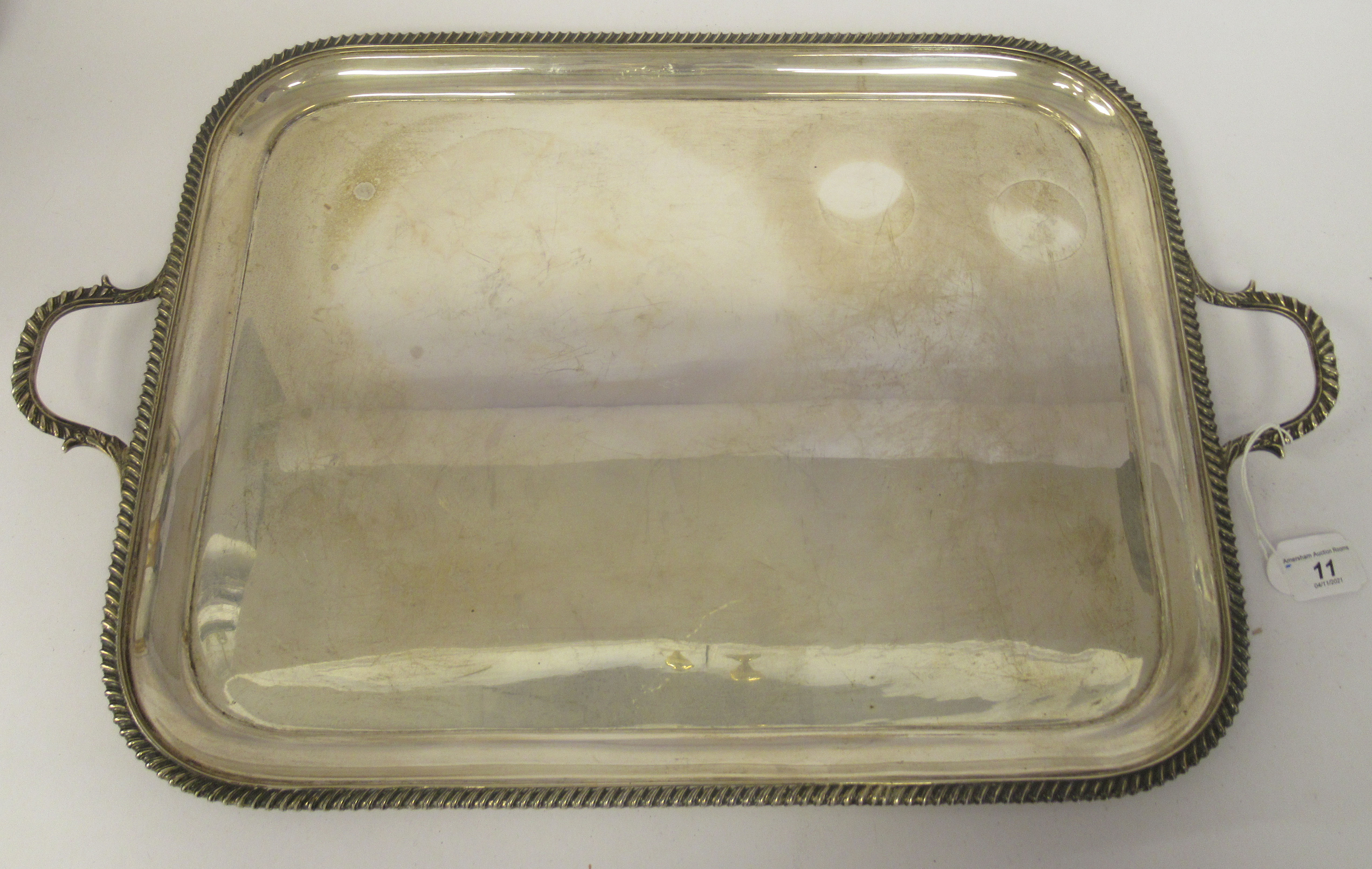 A silver serving tray with a raised gadrooned border and opposing carrying handles  indistinct