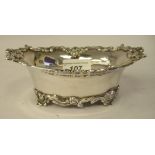 An Edwardian silver oval shallow sweet dish, the flared rim cast with flora and scrolls, on a