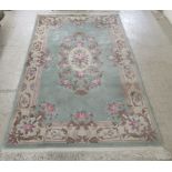 A Chinese washed woollen rug, decorated in traditional floral designs in pale green and pastel