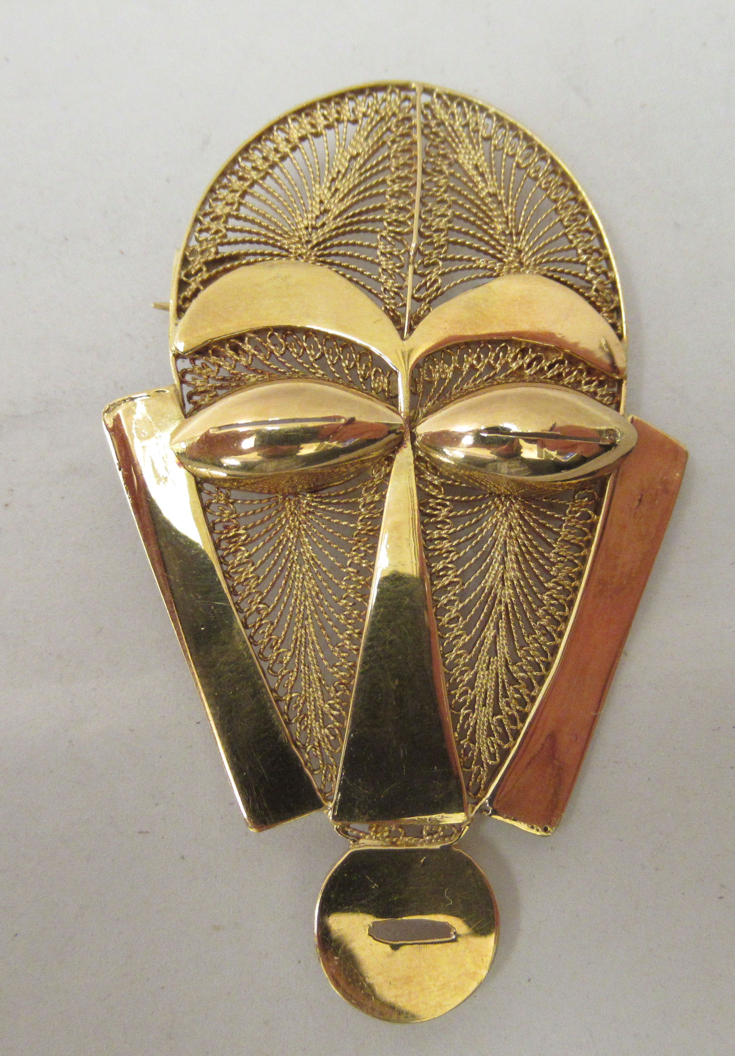 An African gold brooch, fashioned as a tribal mask with filigree ornament  stamped 18ct
