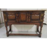 A 20thC Old English style oak sideboard/cabinet with a pair of panelled doors, raised on ring turned