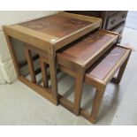 A nesting set of three modern teak framed tile top occasional tables, raised on block legs