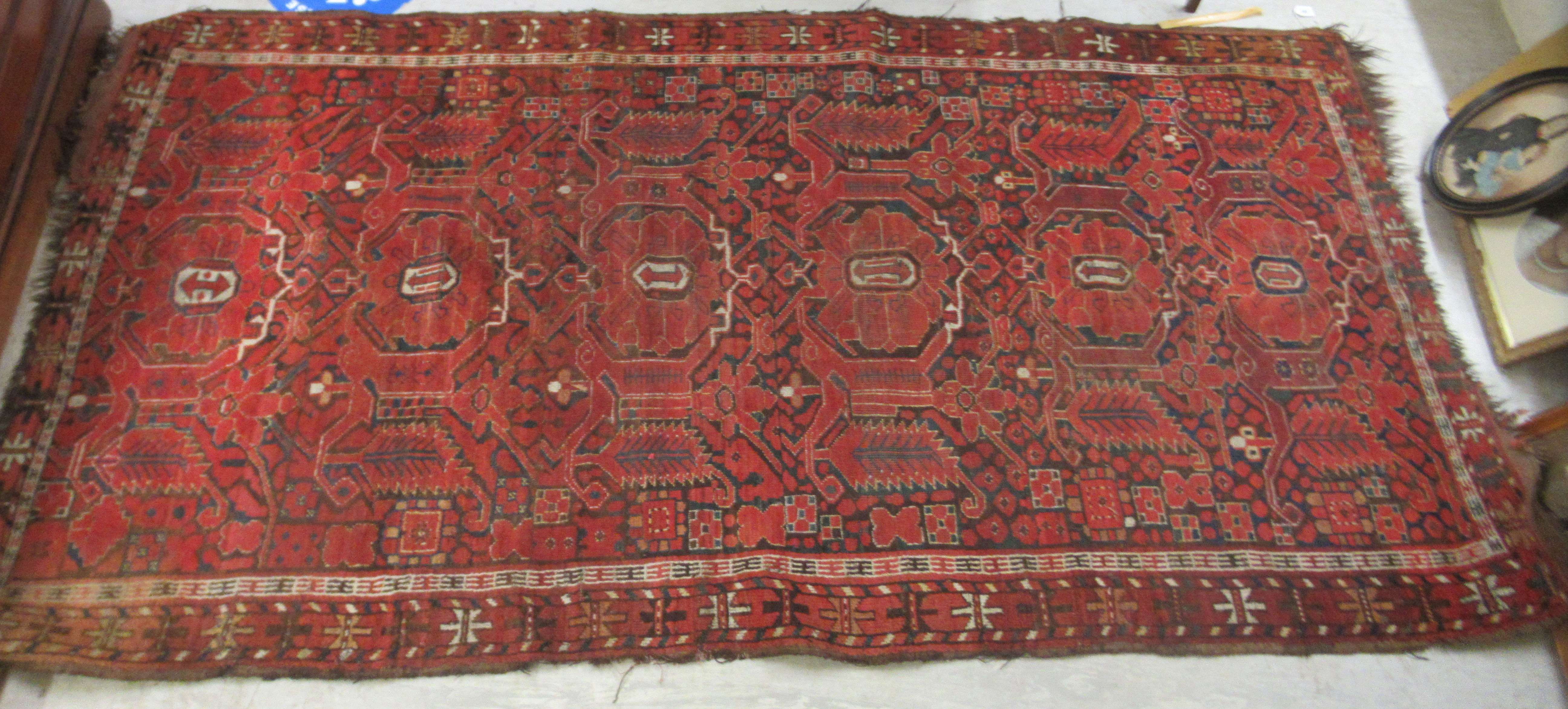 A Turkoman rug, decorated with repeating, stylised designs, on a red ground  97" x 50"