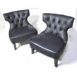 A pair of designer faux black leather easy chairs.