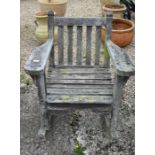 A weathered slatted teak garden rocking armchair