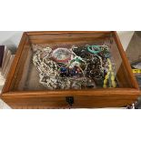 A table top display cabinet containing assorted costume jewellery including necklaces,