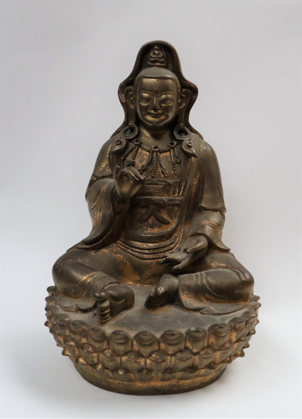 A Bronze figure of Quan yin, seated with right hand raised and left hand resting on her leg,