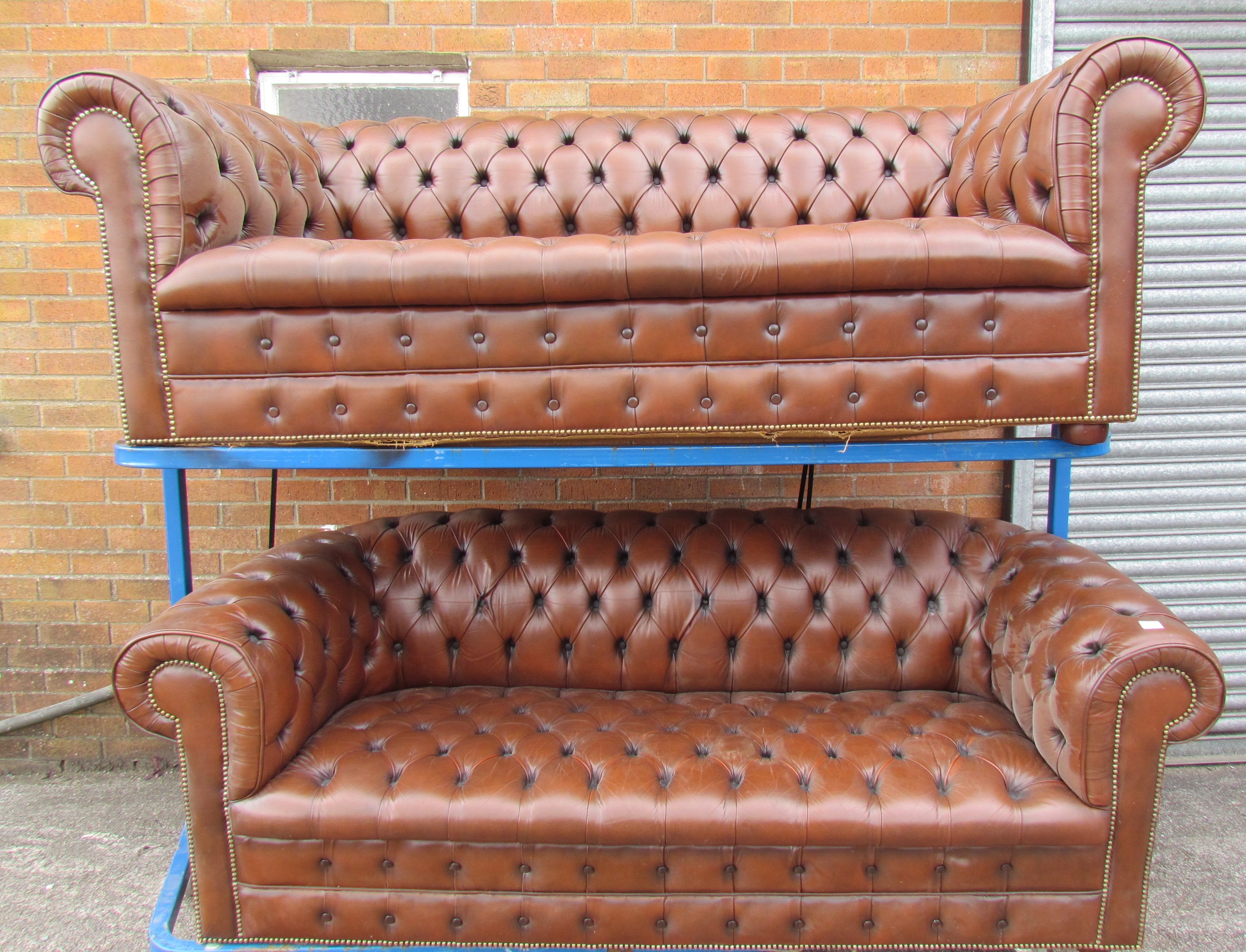 A pair of brown leather chesterfield three seater settees on bun feet