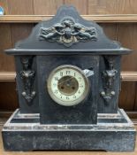 A black slate mantle clock, with a serpentine shaped top with cherubs,