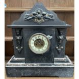 A black slate mantle clock, with a serpentine shaped top with cherubs,