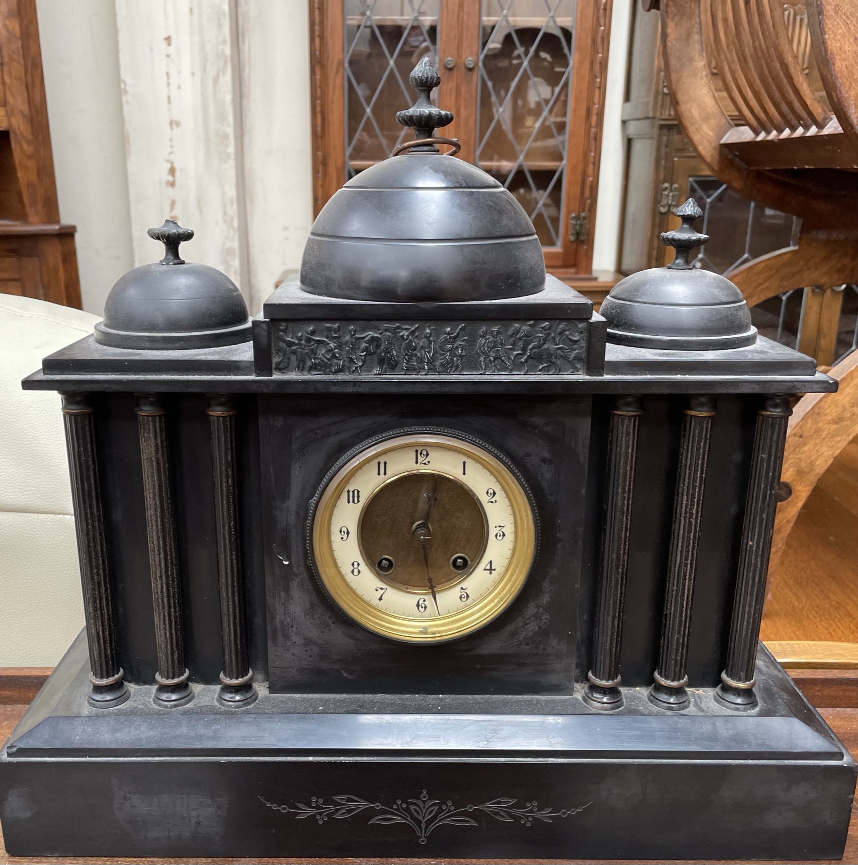 A black slate mantle clock with three domes above an architectural front and plinth base,