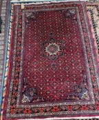 A red ground Persian rug, with interlaced flowers and leaves, the border decorated with roses,