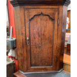 An 18th century oak hanging corner cupboard with a moulded cornice above an ogee panelled door