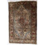 A Persian silk rug, with a red ground decorated with interlocking flowerheads and leaves,