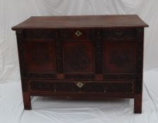 An oak coffer the rectangular moulded top above a carved three panel front and base drawer on
