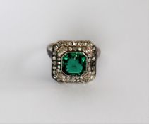 A dress ring set with diamonds and a princess cut green stone to a white metal setting and shank,