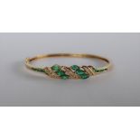 A 14ct yellow gold emerald and diamond set hinged bangle,