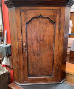 An 18th century oak hanging corner cupboard with a moulded cornice above an ogee panelled door