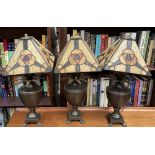 A set of three bronze vase and pineapple table lamps on paw feet with Tiffany style shades