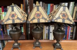 A set of three bronze vase and pineapple table lamps on paw feet with Tiffany style shades