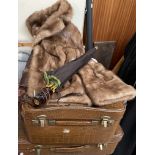 A short brown fur jacket together with two suitcases and an umbrella