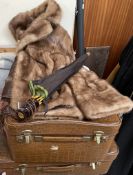 A short brown fur jacket together with two suitcases and an umbrella