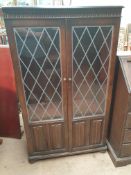 An oak bookcase with leaded glass doors and linen fold panels,