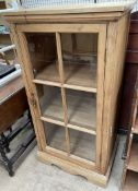 A pine side cabinet with a square top above a glazed door on bracket feet