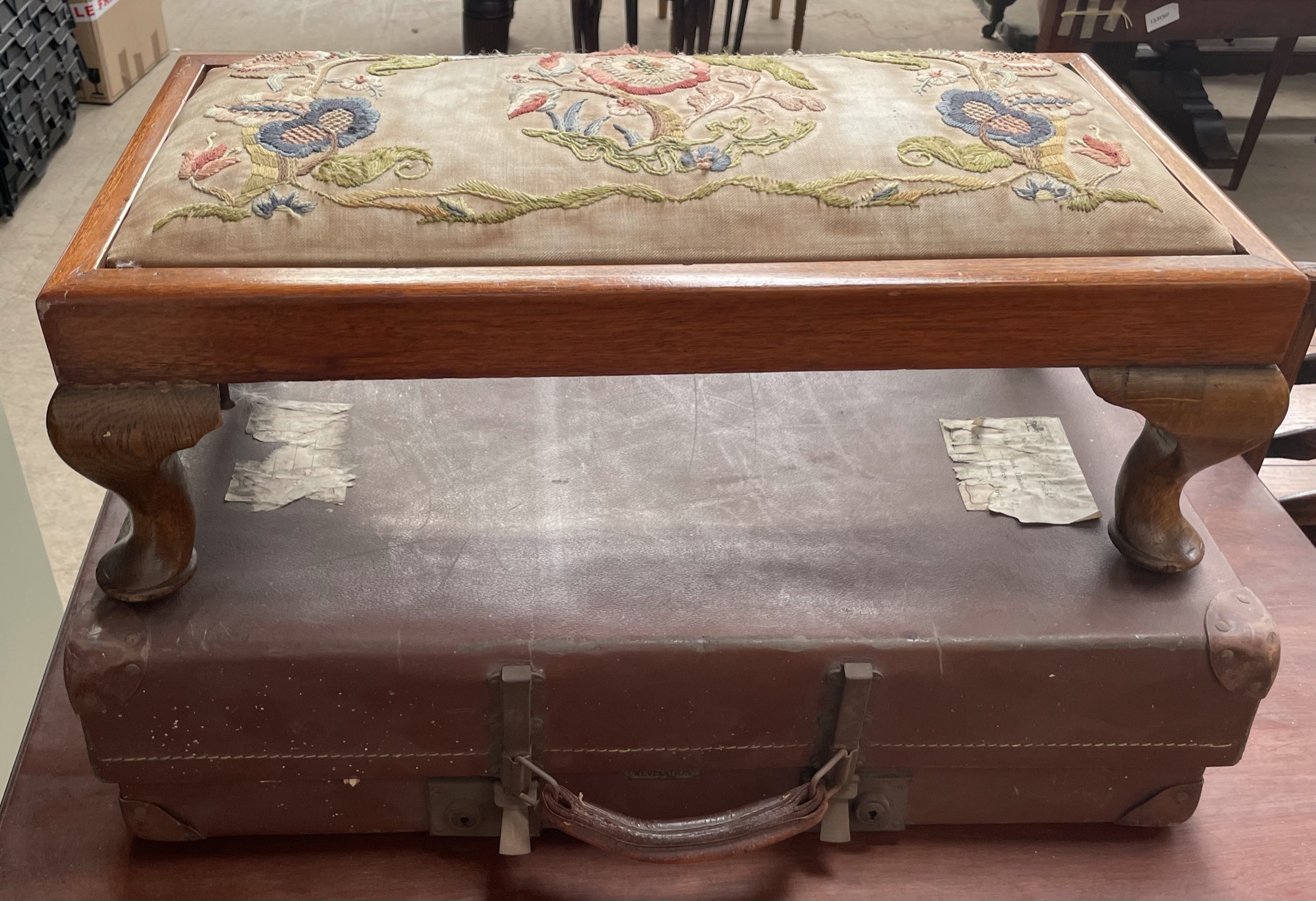 A footstool with embroidered top on cabriole legs together with a suitcase