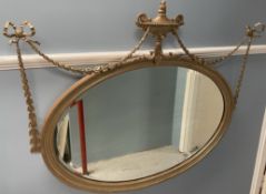 A gilt framed wall mirror of oval form with a central vase and swags