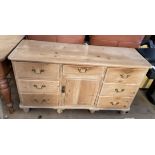A Victorian pine dresser base with an arrangement of drawers and a central cupboard on turned feet