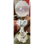 A continental porcelain oil lamp, encrusted with flowerheads and leaves, with a glass globe shade,