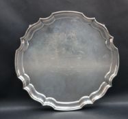An Elizabeth II silver salver of circular form, with a shaped edge on four scrolling feet,