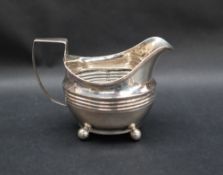 A 19th century silver cream jug, with a line rim and ribbed body on four ball feet,