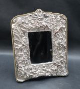 A silver plated easel mirror, profusely decorated with cherubs, flowers and leaves,