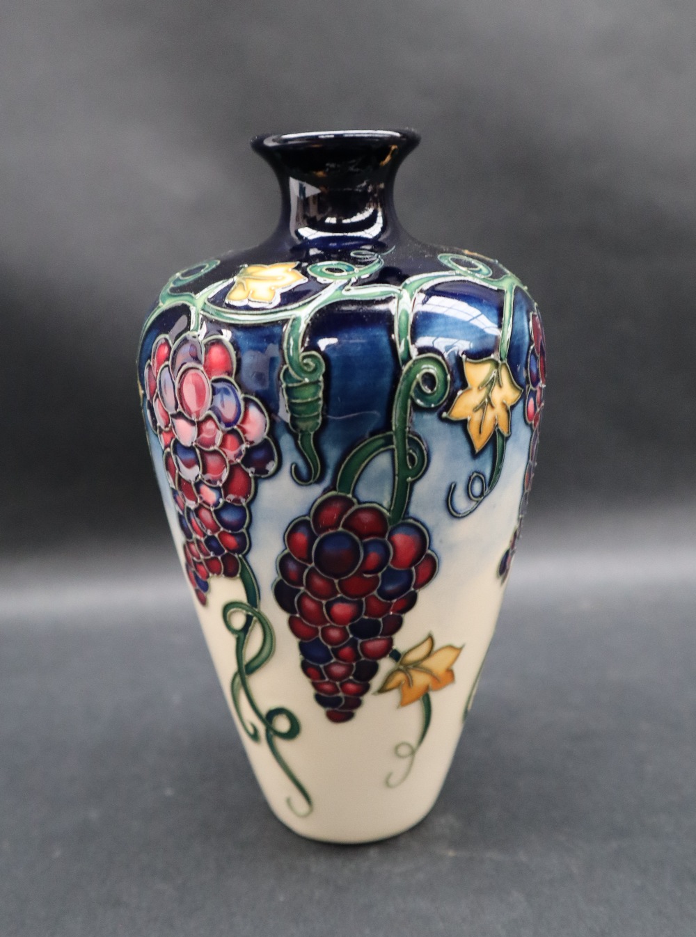 A Moorcroft pottery vase decorated with bunches of grapes and leaves to a cream ground,