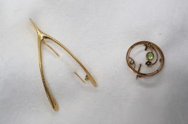 A yellow metal wishbone brooch, together with a 9ct yellow gold peridot and seed pearl brooch,