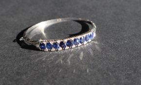 An 18ct white gold sapphire and diamond hinged bangle set with nine oval faceted sapphires and