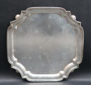 A George V silver salver of square form with shaped corners on ball feet, Sheffield, 1933,