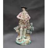 A Derby porcelain figure in a tricorn hat and pink frock coat leaning against a tree stump and