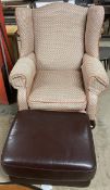 An upholstered wing back elbow chair together with a leather footstool