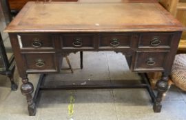 An oak desk with a leather inset top and four drawers on cup and cover legs united by a stretcher