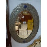 An arts and crafts style oval bevelled wall mirror in a worked pewter frame with blue porcelain