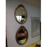 A pair of oval bevelled wall mirrors in matching gilt and green frames each, with a ribbon surmount.