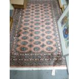 A modern Eastern rug in Turkoman style woven with guls on a pink ground [by silver-plate shelves] TO