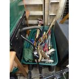 A green garden pull along trolley containing gardening tools including spades, scythes, loppers,