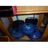 A set of blue Le Creuset cookware comprising three cooking pots with lids and two griddle pans, a