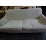A substantial and comfortable settee with cream loose covers and scrolled arms on turned legs and