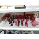 A shelf of cranberry and ruby glass, antique and later, including a decanter with stopper, covered