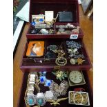 A red folding jewel box containing a good selection of costume jewellery including enamelled